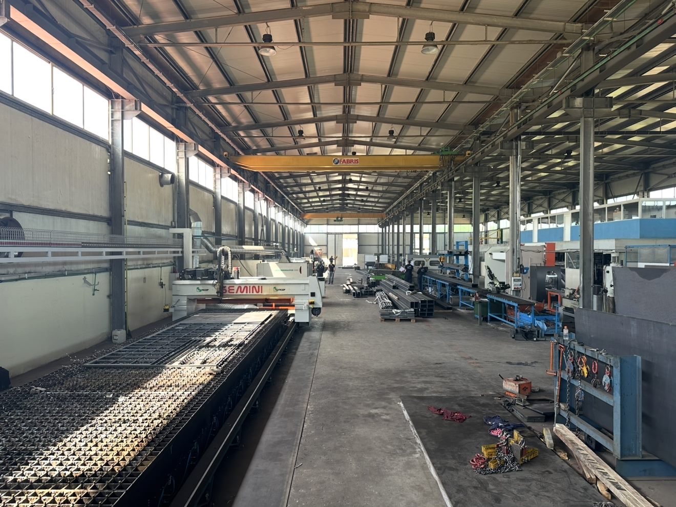 Reparto produttivo Alpantek a Durazzo: tavolo plasma CNC Gemini in primo piano, carroponte e profilati in acciaio sul lato destro.