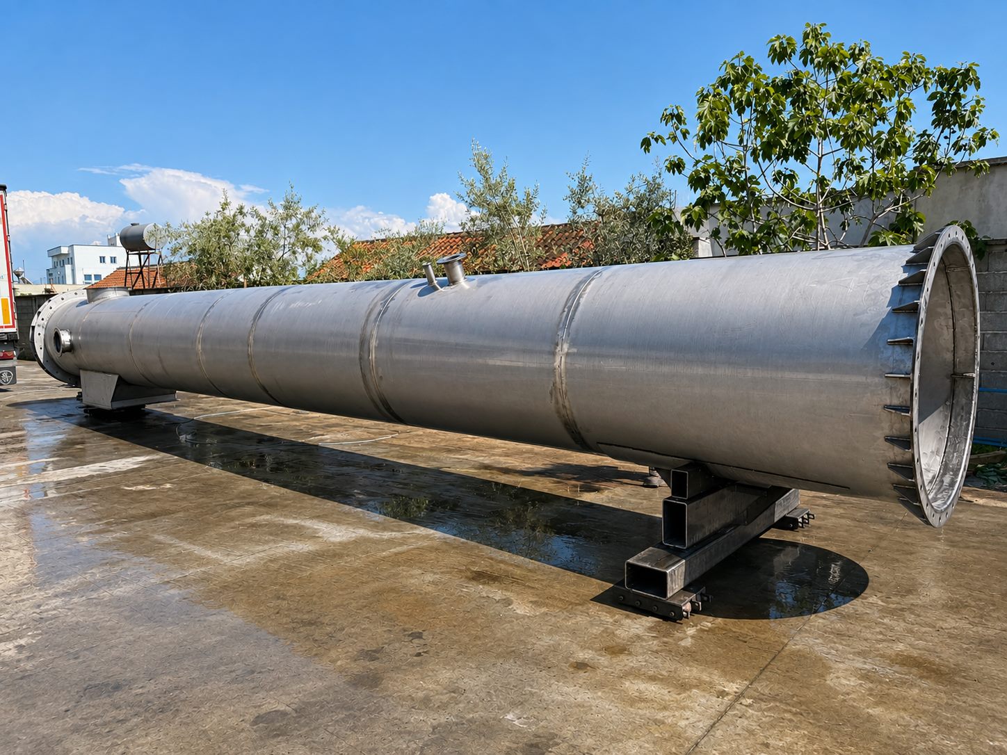 A stainless-steel process vessel standing on fabricated saddle supports: rolled shell with circumferential weld seams, side nozzles and an open flanged end with a bolt-hole backing ring.